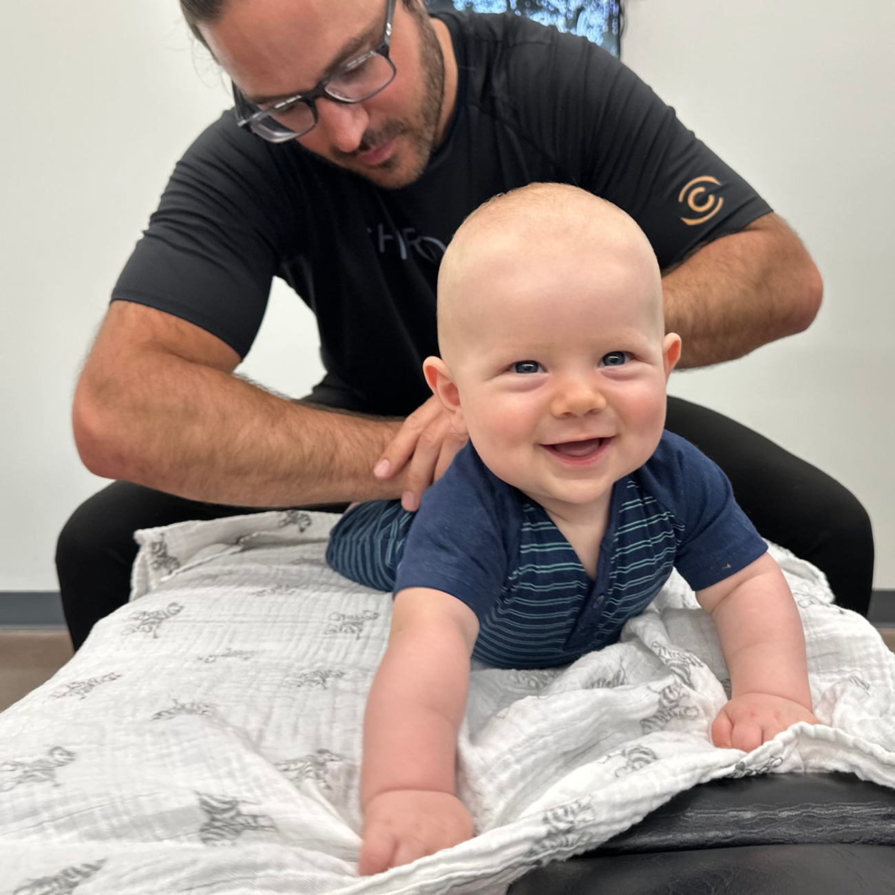 Smiling chiropractor gently adjusting a young child’s back during a pediatric chiropractic visit focused on enhancing well-being and promoting healthy development.